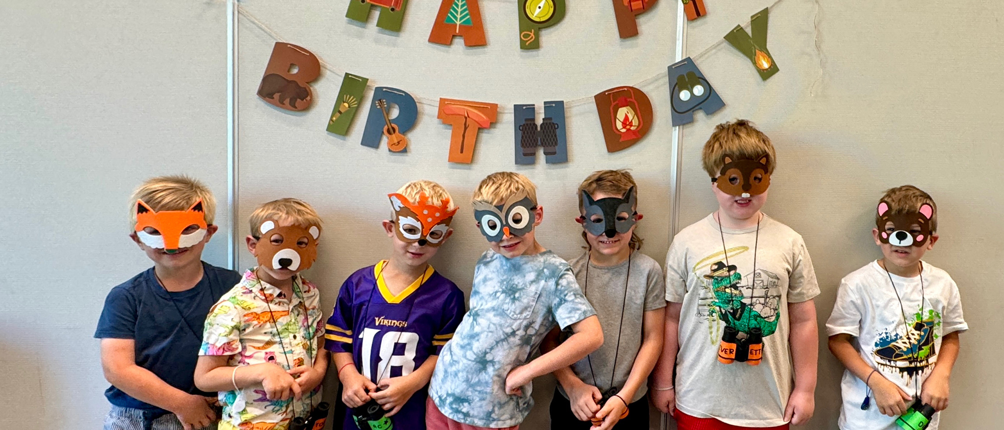 Kids in a line wearing masks in front of a Happy Birthday sign.